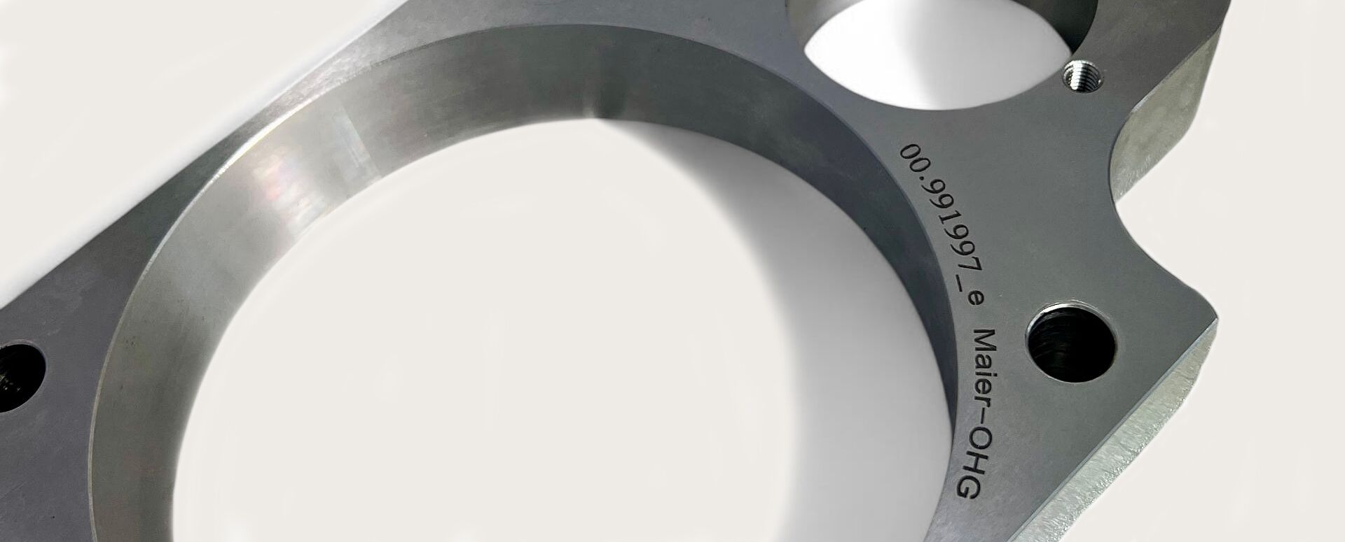 Präzise gefrästes Metallbauteil mit mehreren Bohrungen und Gewinden, auf einer metallischen Arbeitsplatte liegend. Die Oberfläche ist glatt, mit sichtbarer Gravur einer Artikelnummer. Technisch und exakt verarbeitet.